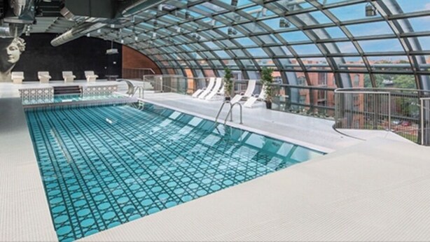 Una piscina interior con techo de vidrio, sillas de descanso y vistas a la ciudad.