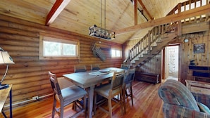 L’intérieur d’un chalet en bois comprend une table à manger, des chaises, un escalier et une cheminée.