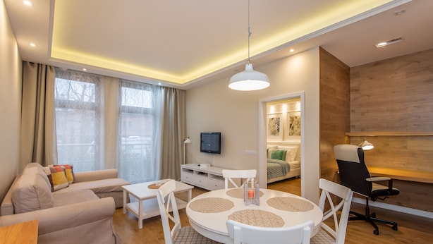 A modern living room with a sofa, a dining table with chairs, a TV, and a wooden accent wall. - Super-Apartamenty City Park II (Poznan)