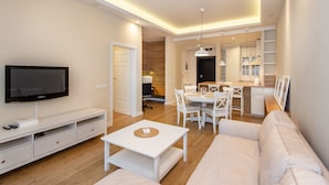 A modern living room with a flat-screen TV, white furniture, a dining area with a table and chairs, and a kitchen in the background. - Super-Apartamenty City Park II (Poznan)