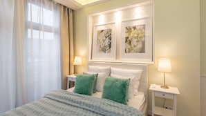 A neatly arranged bedroom with a bed, two green pillows, a bedside table with a lamp, and two framed floral artworks on the wall. - Super-Apartamenty City Park II (Poznan)