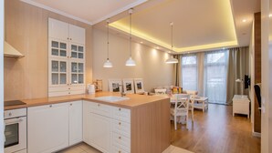 A modern kitchen with white cabinetry, a central island, pendant lighting, and a dining area with a white table and chairs. - Super-Apartamenty City Park II (Poznan)