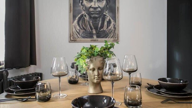 A dining table set with plates, bowls, and wine glasses, a bust sculpture centerpiece, and a framed portrait on the wall.