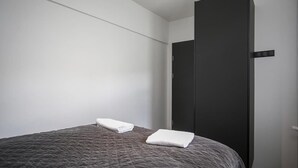 A single bed with a dark textured bedspread and two neatly folded white towels.