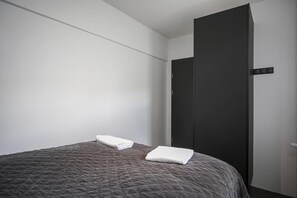 A single bed with a dark textured bedspread and two neatly folded white towels.