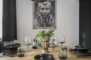 A dining table set with plates, bowls, and wine glasses, a bust sculpture, and a potted plant.