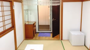 A traditional Japanese room with tatami flooring, a shoji screen door, a small wooden table, and a white air conditioning unit. - Guanjing Apartment (Tokyo)