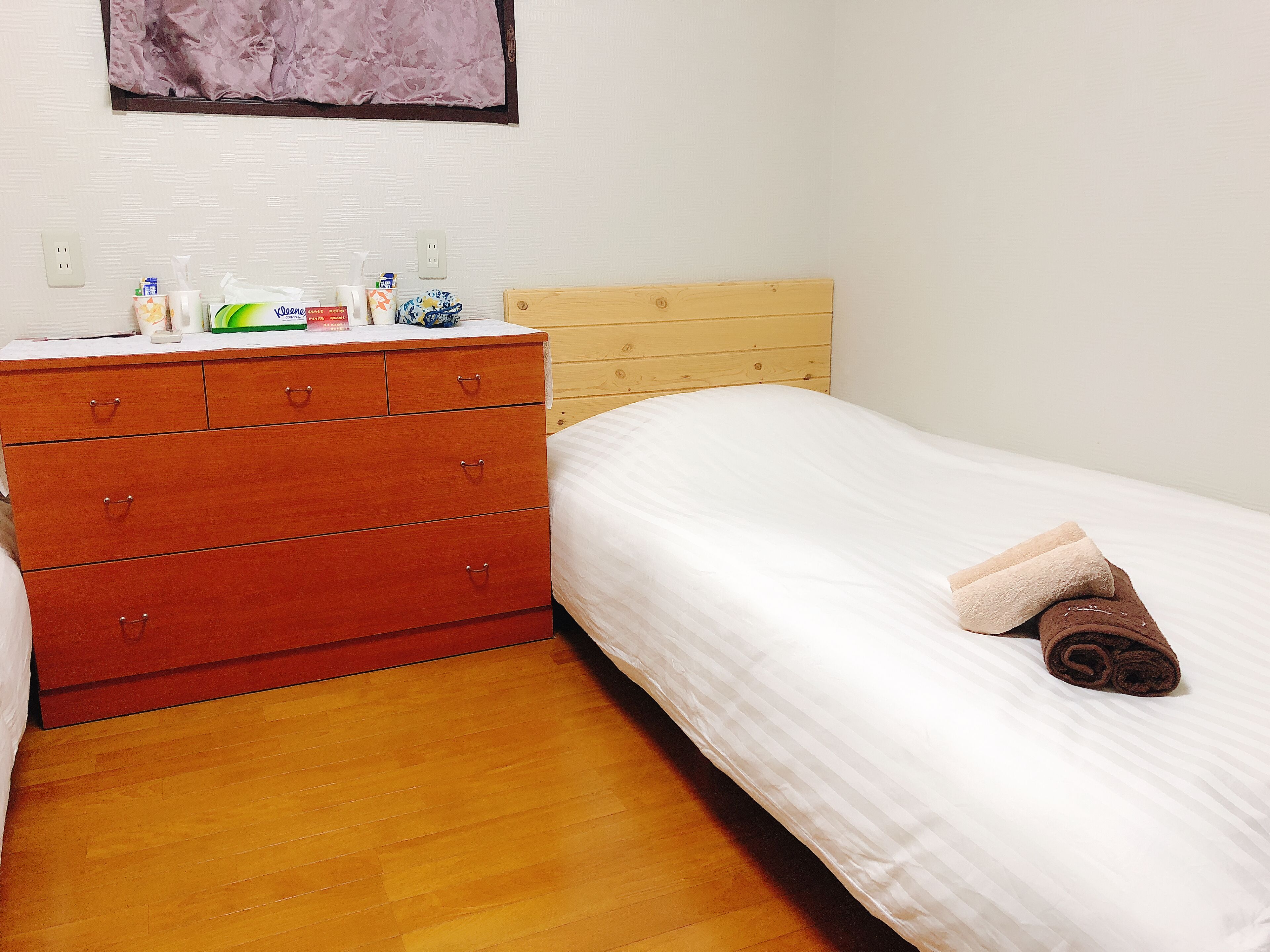 A bedroom with a wooden dresser, a bed with a white comforter, and a wooden headboard.