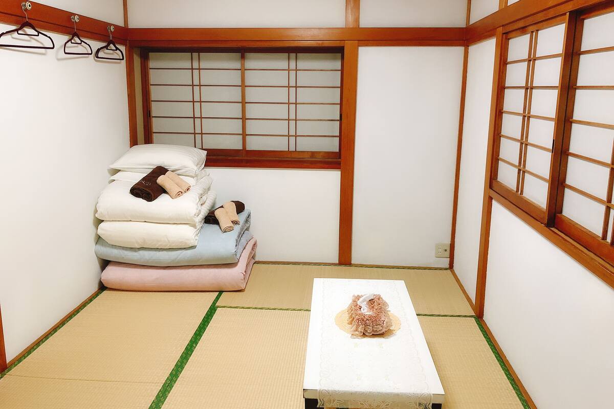 A traditional Japanese room with tatami flooring, a futon bed, a small table with a decorative item, and a shoji screen window.