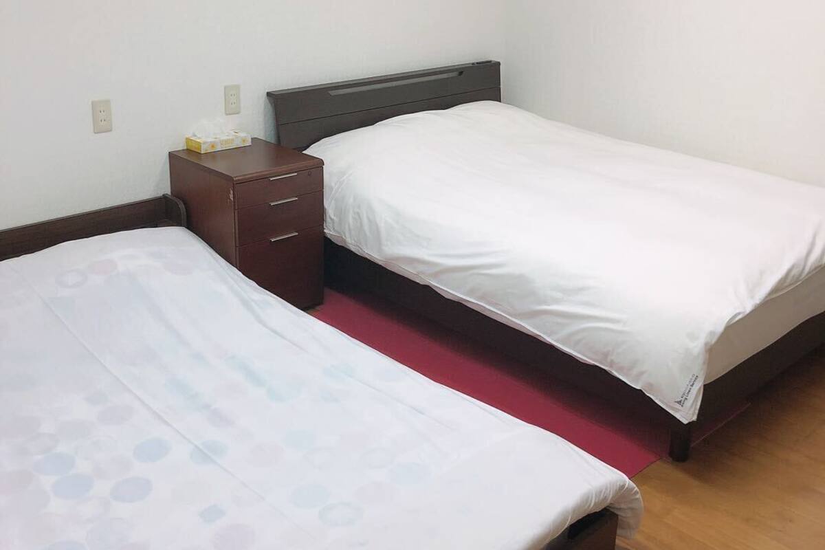 A hotel room with two single beds, a wooden dresser, and a red carpet.