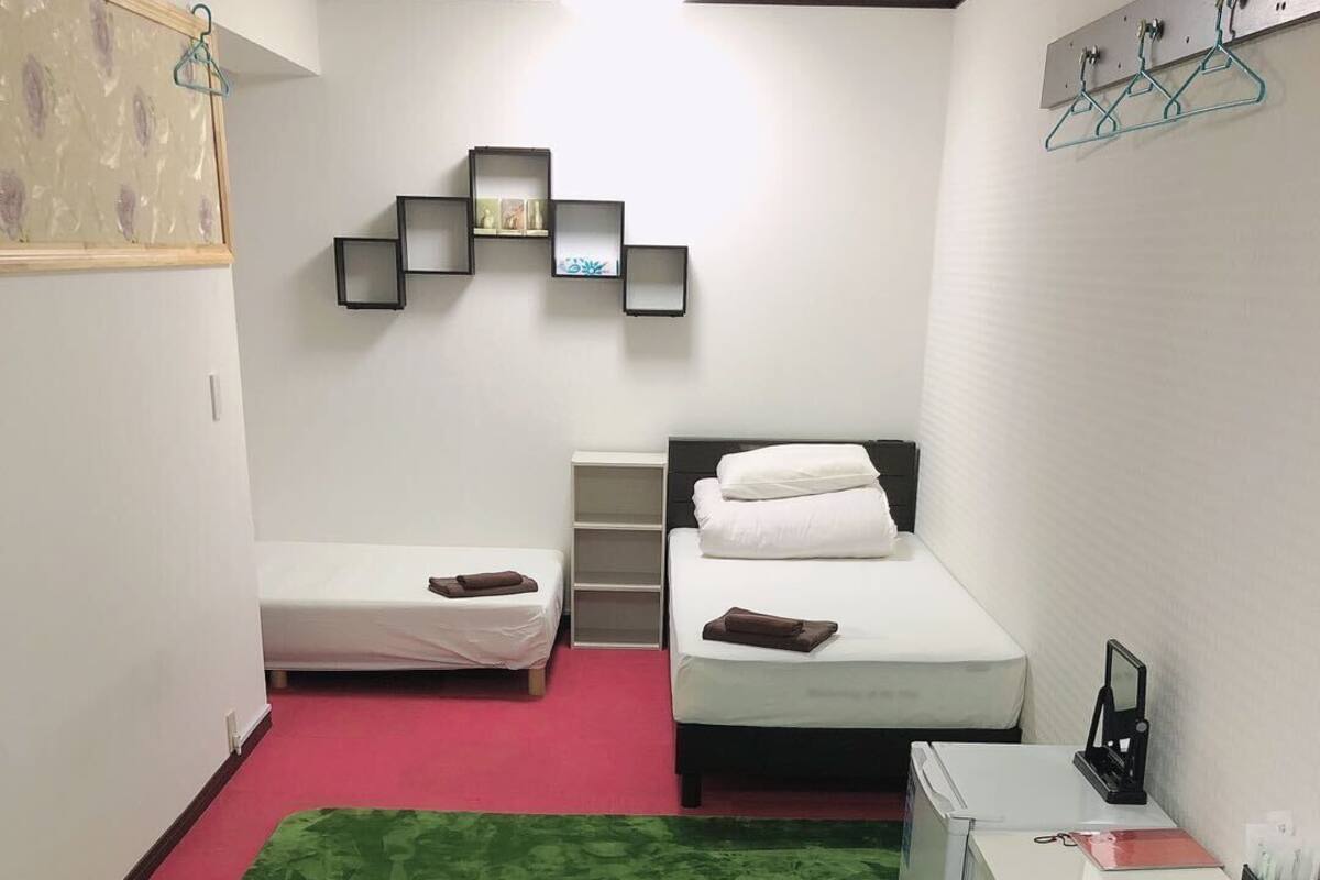 A hotel room with two beds, a desk, a chair, a green carpet, and a wall-mounted shelf with a picture.