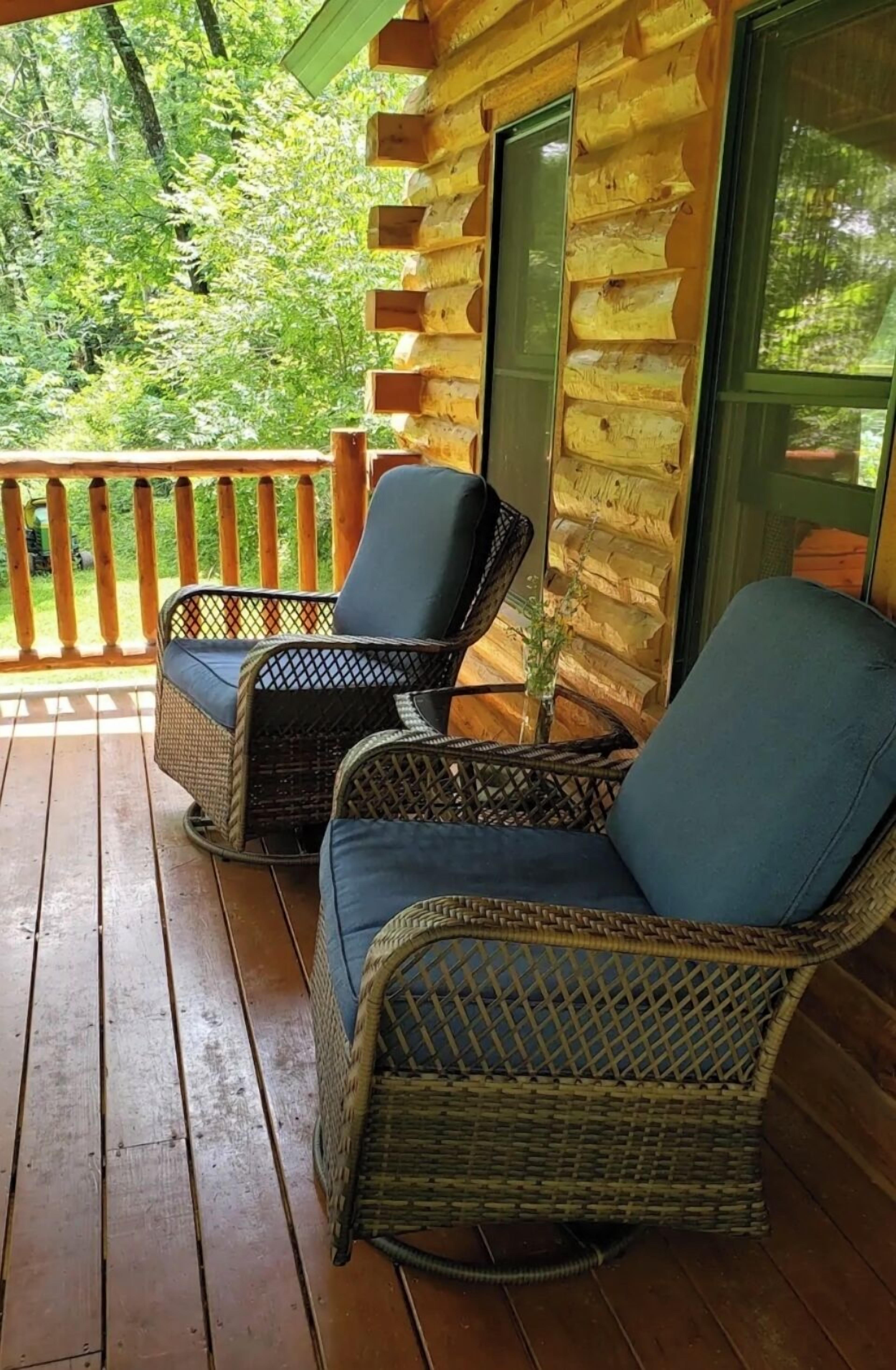 A wooden cabin with a porch featuring wicker chairs with cushions.