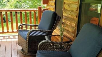 A wooden cabin with a porch featuring wicker chairs with cushions.