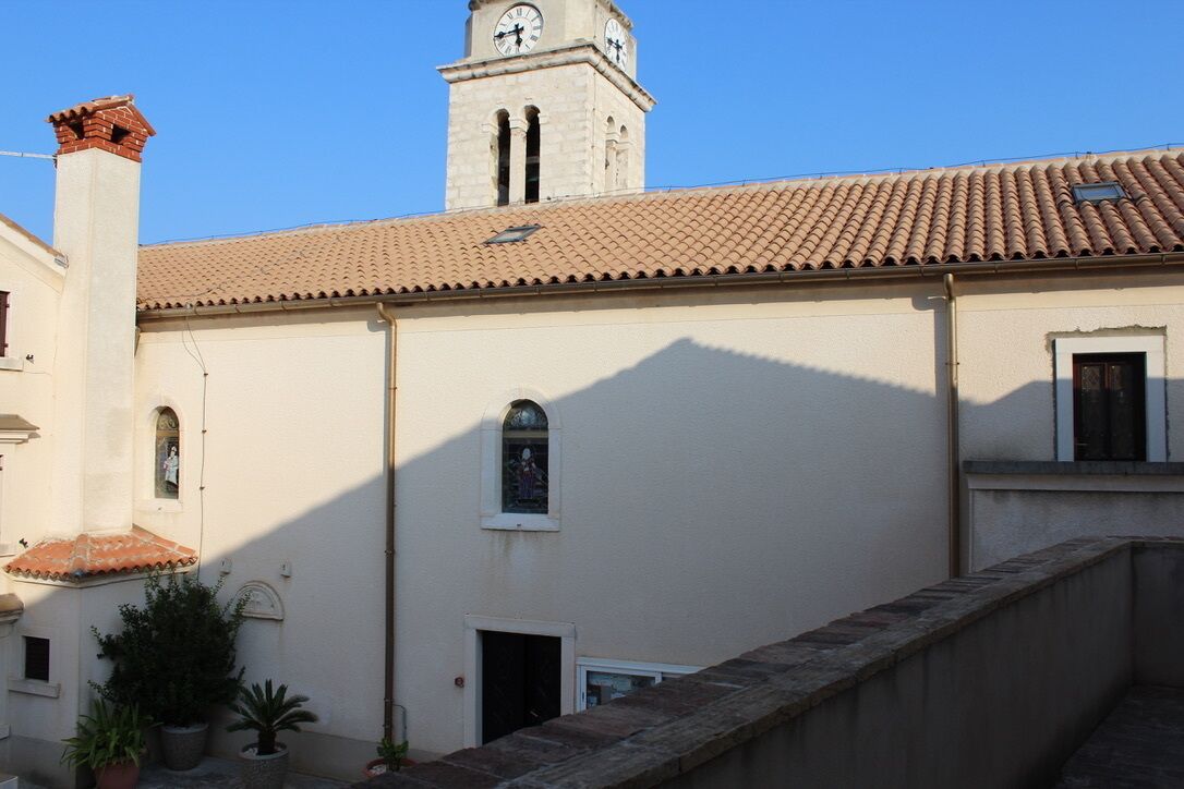 A building with a clock tower, a tiled roof, and a small window with a statue.