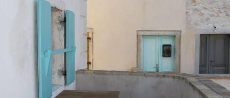 A narrow alleyway with a wooden table and a light blue door, surrounded by stone walls.