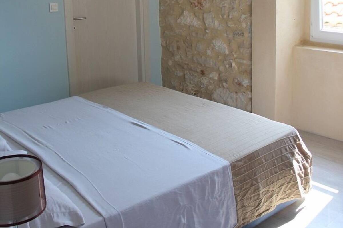 Ein Schlafzimmer mit Bett, einem angebrachten Fernseher, einer Tür und einem Fenster mit Ausblick.