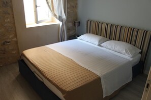Een net opgemaakt bed met een gestreept hoofdeinde, een bedlampje en een raam met gordijnen.