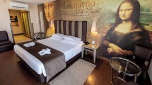 Une chambre d’hôtel avec un lit, une chaise, une table et un mur orné d’un tableau célèbre.
