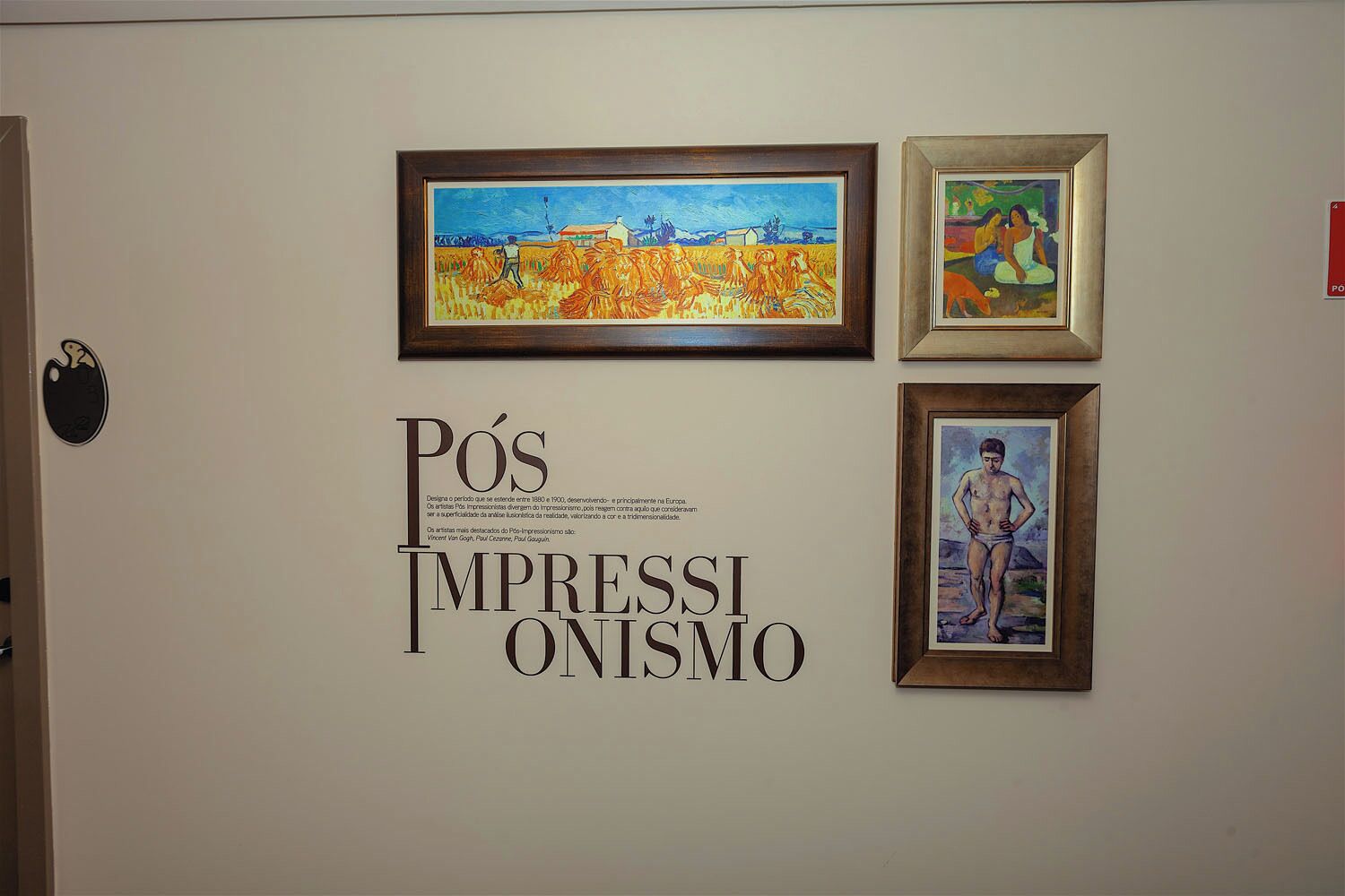 A wall with three framed artworks and a sign with the text 'PÓS IMPRESSIÃO.'