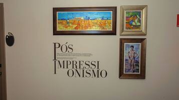 A wall with three framed artworks and a sign with the text 'PÓS IMPRESSIÃO.'
