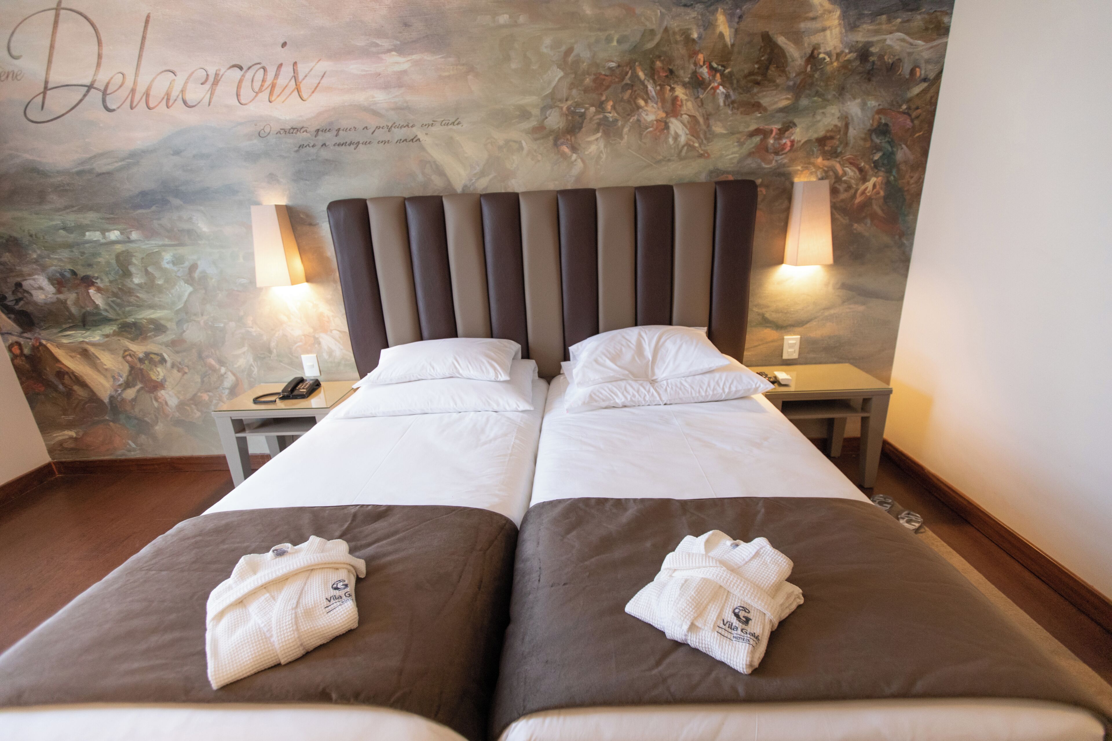 A hotel room with two beds, a headboard, bedside lamps, a phone, and a wall mural.