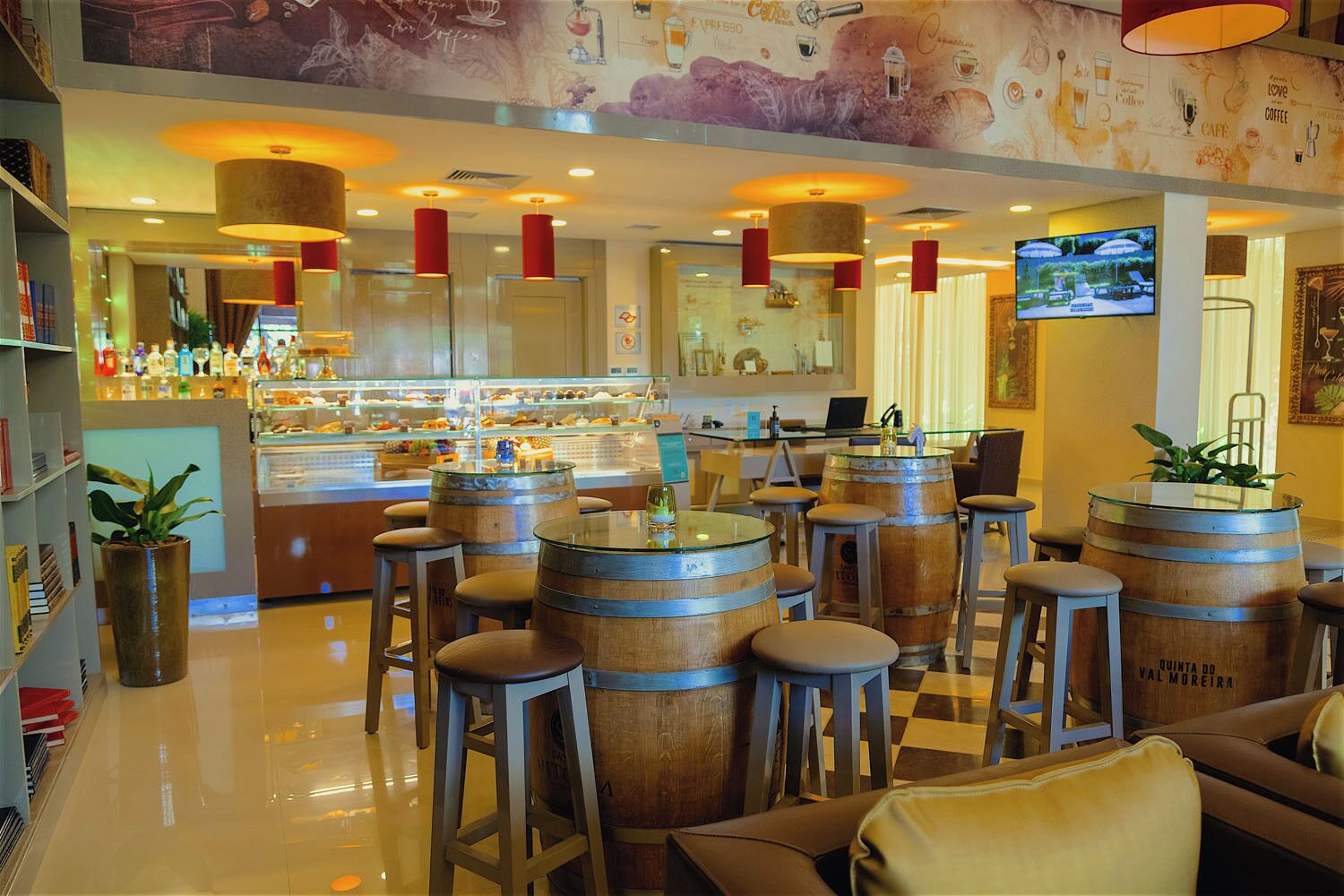 Zona de bar con barriles de madera como taburetes, barra con diversas botellas y una pantalla de televisión.
