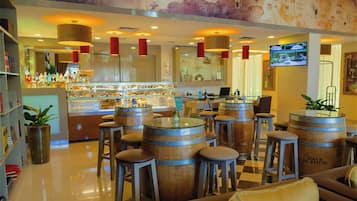 Zona de bar con barriles de madera como taburetes, barra con diversas botellas y una pantalla de televisión.
