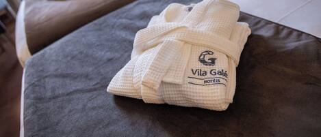 A neatly folded bathrobe with a logo on it, placed on a dark-colored bed with white sheets.
