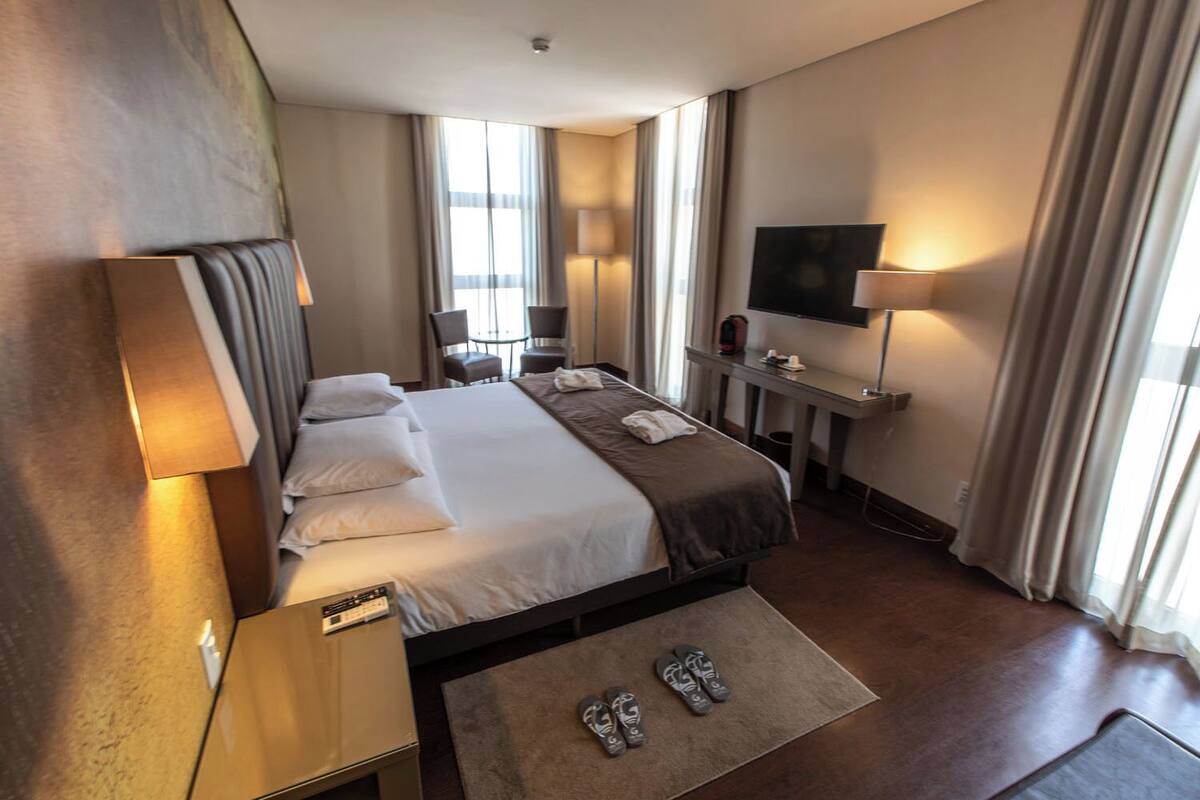A hotel room with a bed, bedside tables, a TV, a desk, and a chair.