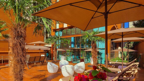 Un patio intérieur doté d’un plancher en bois, de sièges blancs rembourrés et de grands parasols offrant de l’ombre.