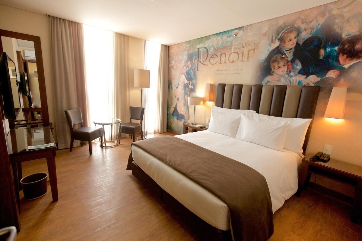 Une chambre d’hôtel avec un grand lit, un bureau avec une chaise, une petite table et un miroir.