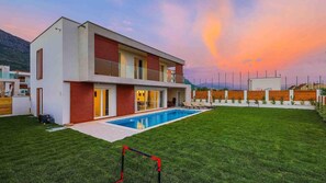 Enjoy a spacious backyard with a swimming pool and lawn, a large open living area, and a balcony with views of the surrounding landscape.
