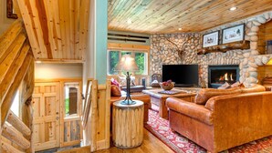 A cozy cabin interior with a stone fireplace, leather sofa, and a television.