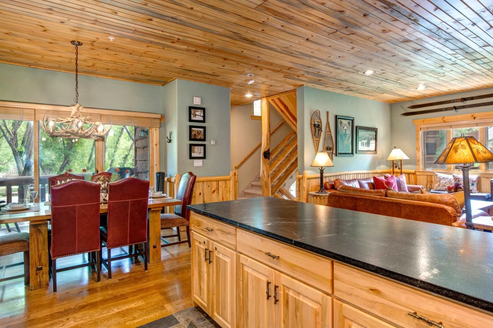 A spacious kitchen with wooden cabinets, a dining area with red chairs, and a cozy seating area with a sofa and cushions.