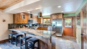 A kitchen with a large island, wooden cabinets, stainless steel appliances, and a stone floor.