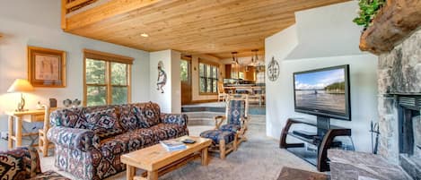 A spacious living room with a high ceiling, a fireplace, a television, and a dining area with wooden furniture.