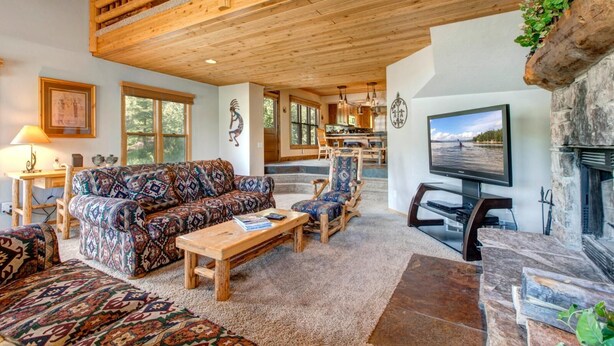 A spacious living room with a high ceiling, a fireplace, a television, and a dining area with wooden furniture.