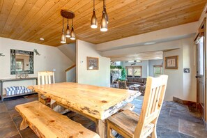 A wooden dining table with benches, a hanging light fixture, and a stone-tiled floor. - Walk to Ski Slopes + Trails! Spacious 4-Bedroom Private Home with Fantastic Views, Hot Tub, A/C, and Wood Fireplace | PLA-1155 by KBM Resorts (Park City)