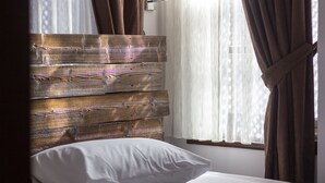 Un letto con biancheria bianca, una testiera in legno e una finestra con tende leggere.