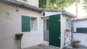 A building with a green door, a window with green shutters, and a small balcony with potted plants.