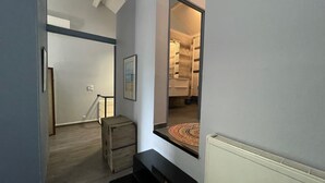 A narrow hallway with a wooden chest, a framed picture on the wall, and a glimpse of a bathroom with a towel rack and a radiator.