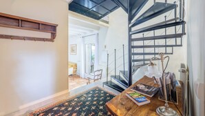 A staircase with a metal railing, a wooden table with books and a lamp, and a patterned rug on the floor.