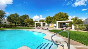 A swimming pool with lounge chairs and a covered seating area, surrounded by trees and a clear sky. - Luxury Studio | Pool, Spa & Fireplace (St. George)