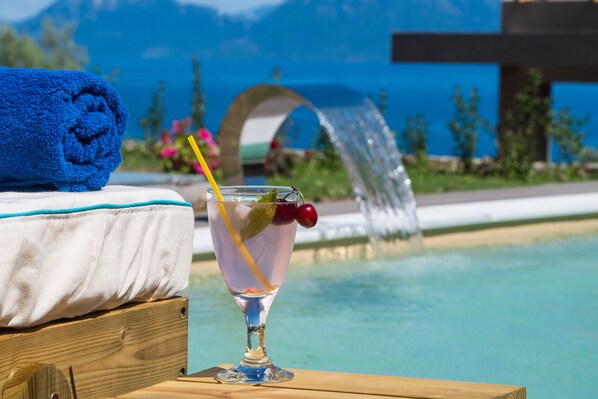 A poolside setting with a clear view of a mountain range, a blue towel, and a glass of a beverage with a straw and cherry garnish.