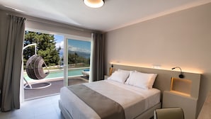 Een moderne hotelkamer met een groot bed, een stoel, een nachtkastje en uitzicht op een zwembad en bergen door de glazen deur.