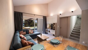 Een moderne woonkamer met een eethoek, een bank, een salontafel en een trap naar een bovenverdieping.
