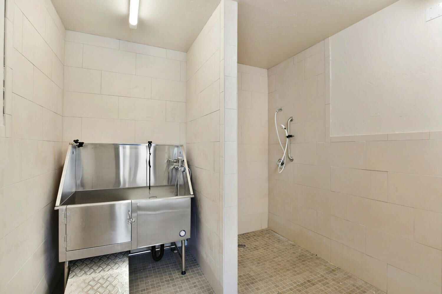 Ein kleines, sauberes Badezimmer mit einem Edelstahlwaschbecken, einer Dusche und gefliesten Wänden.