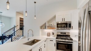 Une cuisine moderne avec des meubles blancs, des appareils en acier inoxydable et des luminaires suspendus.