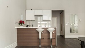 A modern kitchen with two white bar stools, a wooden countertop, and a potted plant. - Modern 1BR Period Property in Kensington (London)