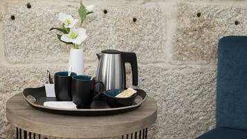 Una mesa redonda de madera con una bandeja que sostiene un jarrón blanco con flores, tazas negras, un hervidor plateado y un bol con pan plano.
